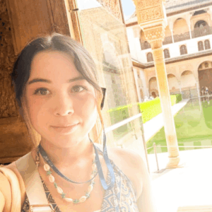 明るい日差しの下、歴史ある建物の前で写っている女性の写真