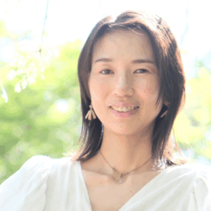 「緑の背景の中、白い服を着た女性がやさしく微笑んでいるポートレート写真