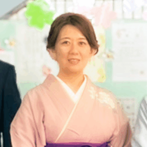 淡いピンク色の和服を着た女性が室内で微笑んで立っている写真