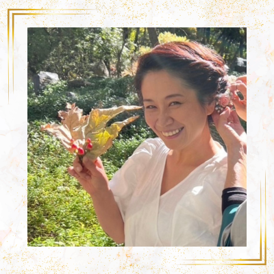 屋外で木の葉を手に持ち、明るい笑顔を見せている女性の写真