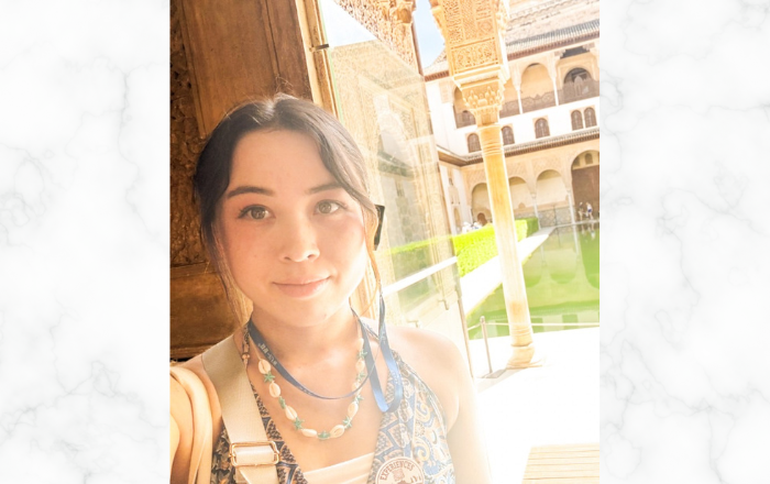 明るい日差しの下、歴史ある建物の前で写っている女性の写真