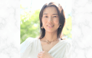 「緑の背景の中、白い服を着た女性がやさしく微笑んでいるポートレート写真