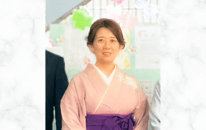 淡いピンク色の和服を着た女性が室内で微笑んで立っている写真